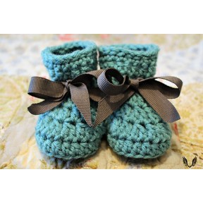 Two blue baby booties with black bows sitting on a yellow blanket